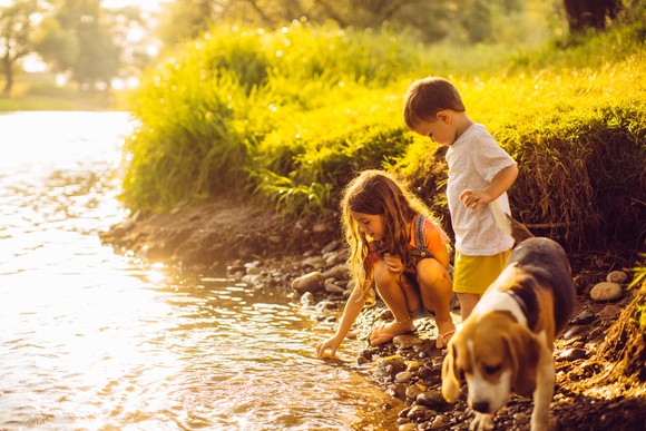 Two children with beagle by a riverbank.