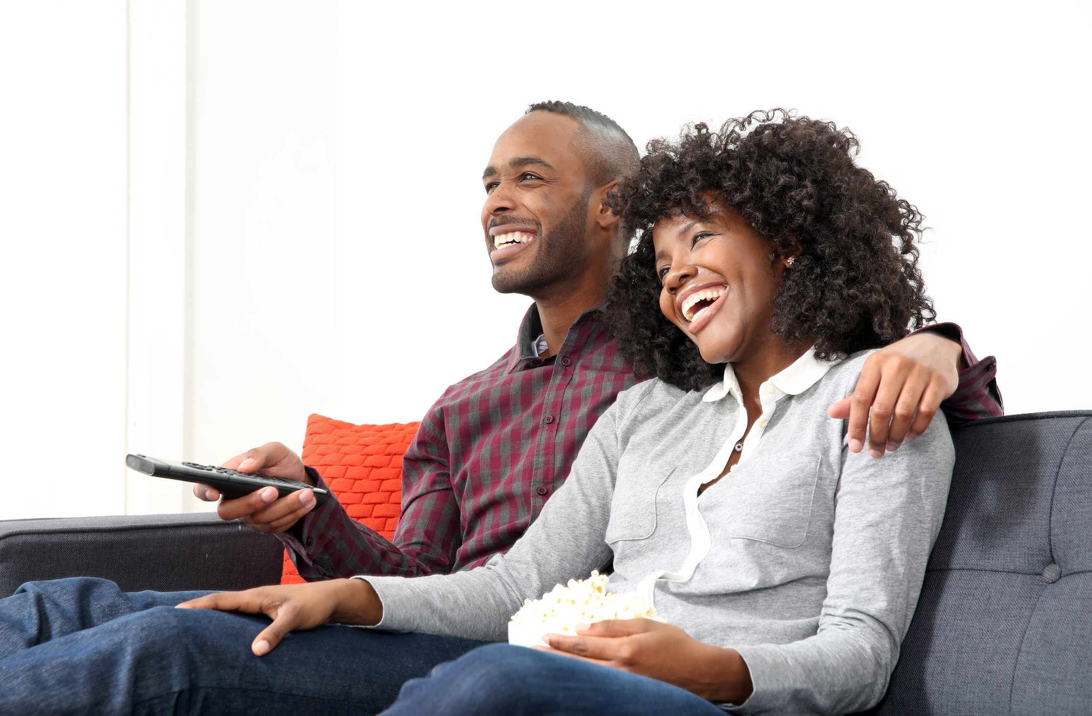 A smiling couple enjoys watching a TV program at home while sitting together on a couch.