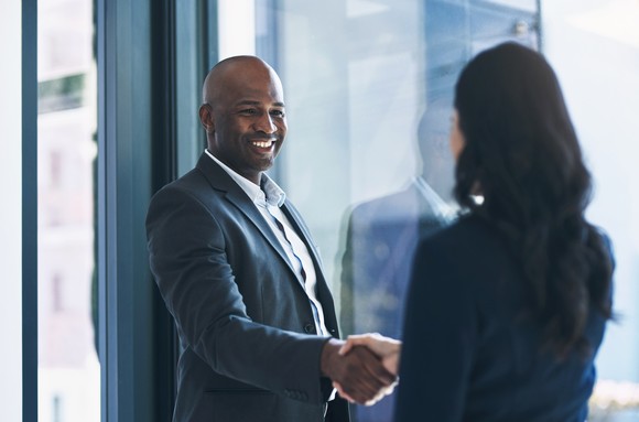 Two people in a corporate office building shake hands.