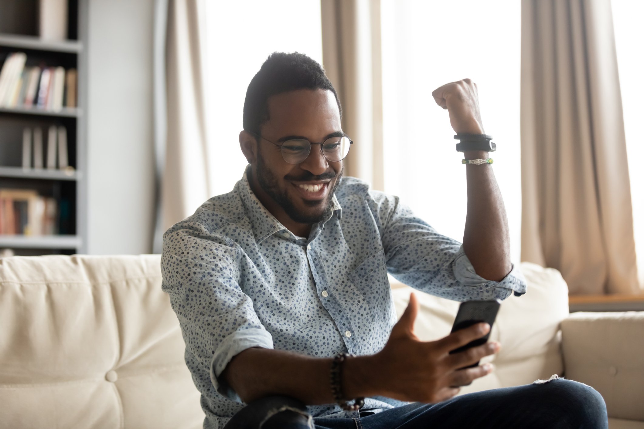A person appears to celebrate while sitting on a couch holding a phone.