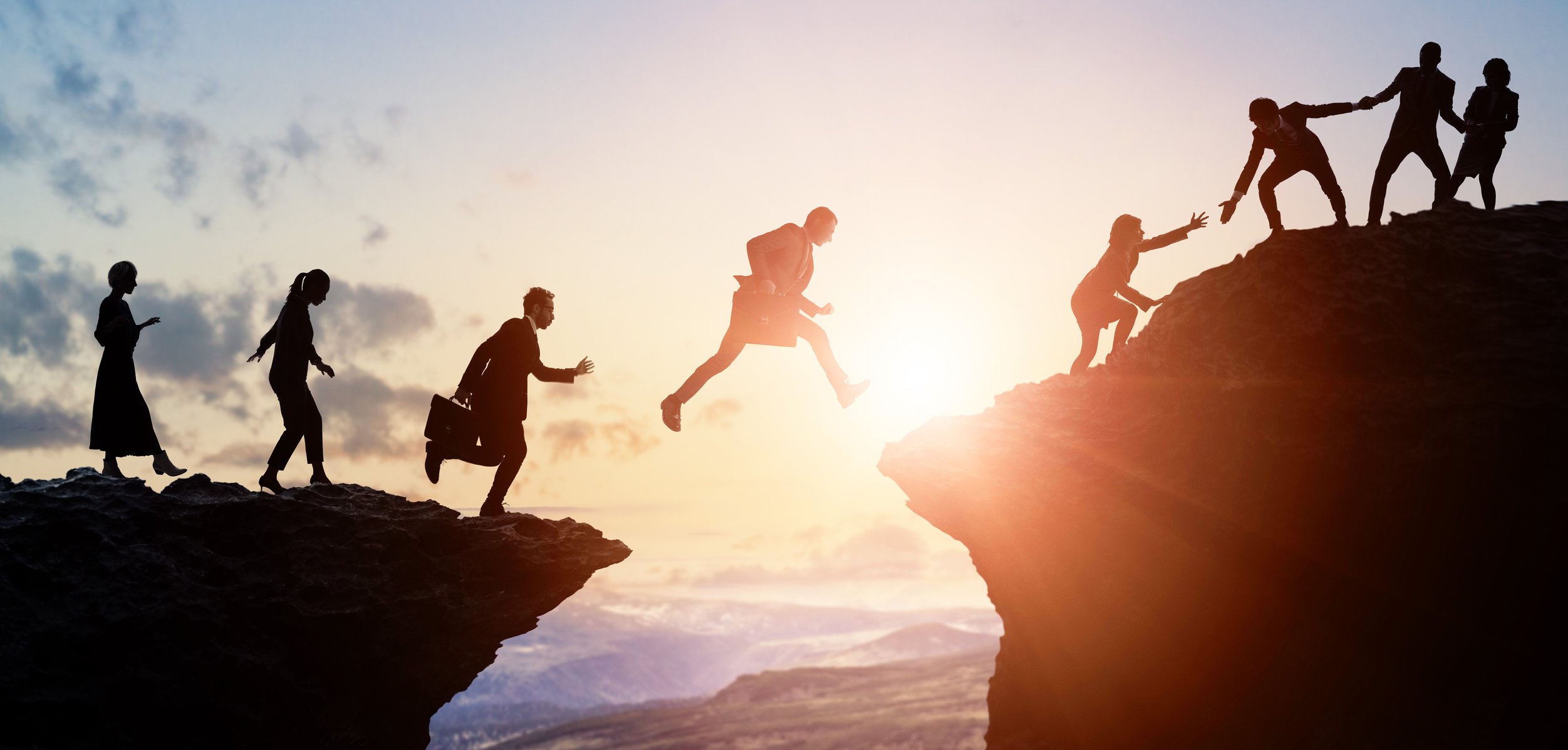 A group of people jumping from one ledge to another on a mountain.