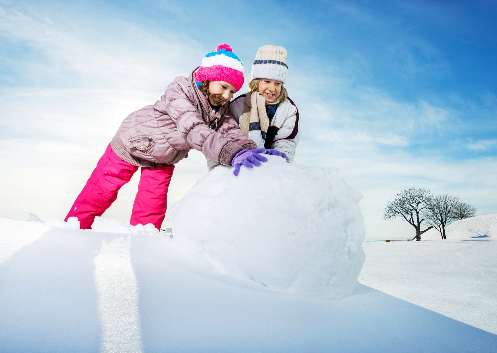 Two children rolling a large snowball. 