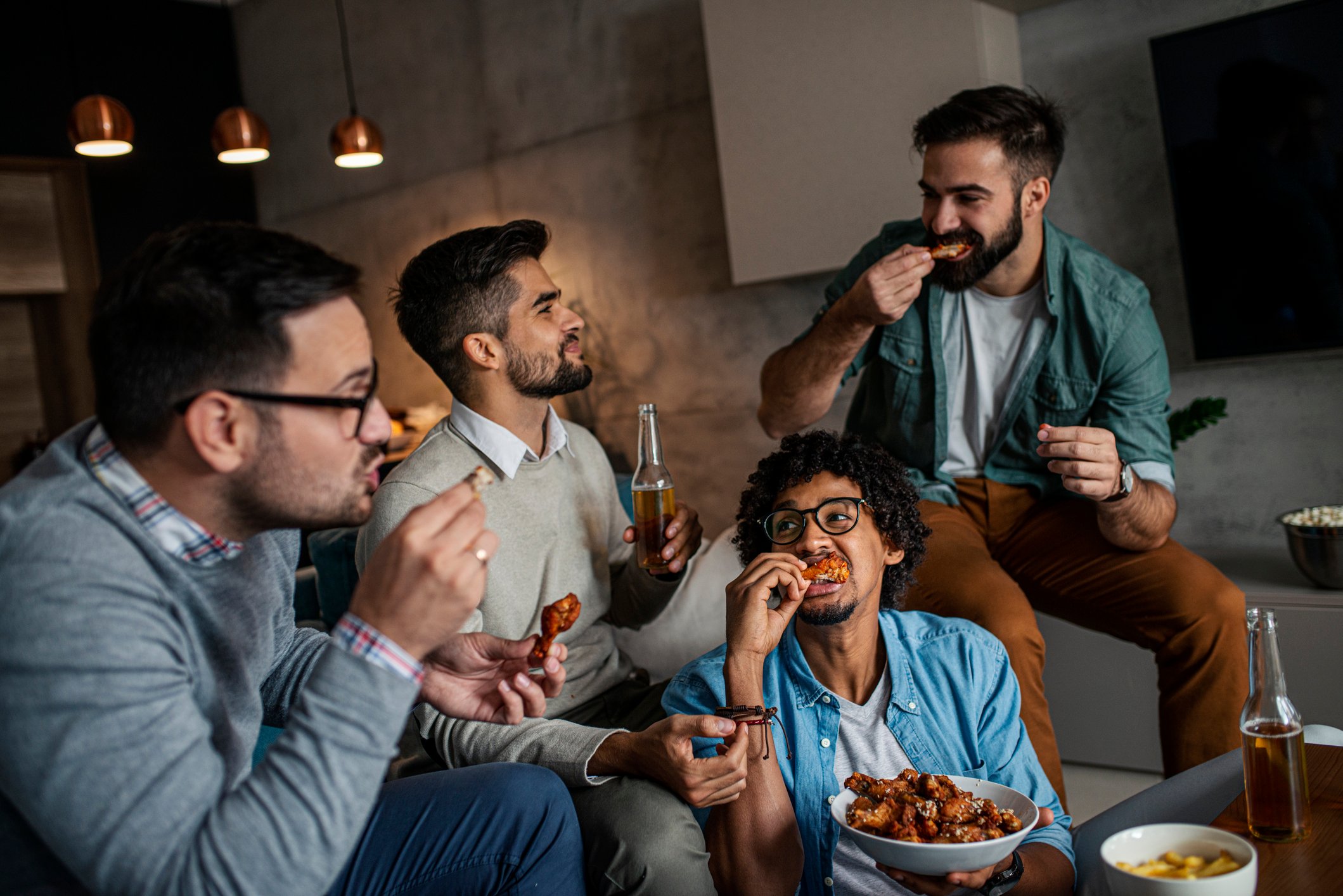 Friends sitting around a coffee table eating chicken wings.
