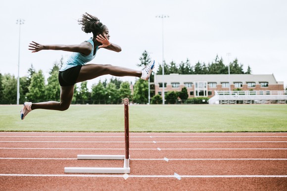 A track runner jumping over a hurdle.