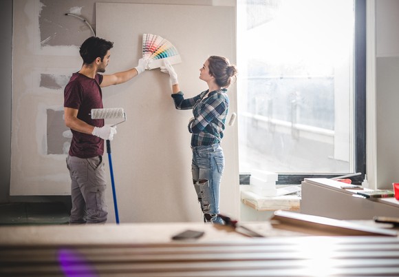 A couple holding swatches against a wall preparing to paint it.
