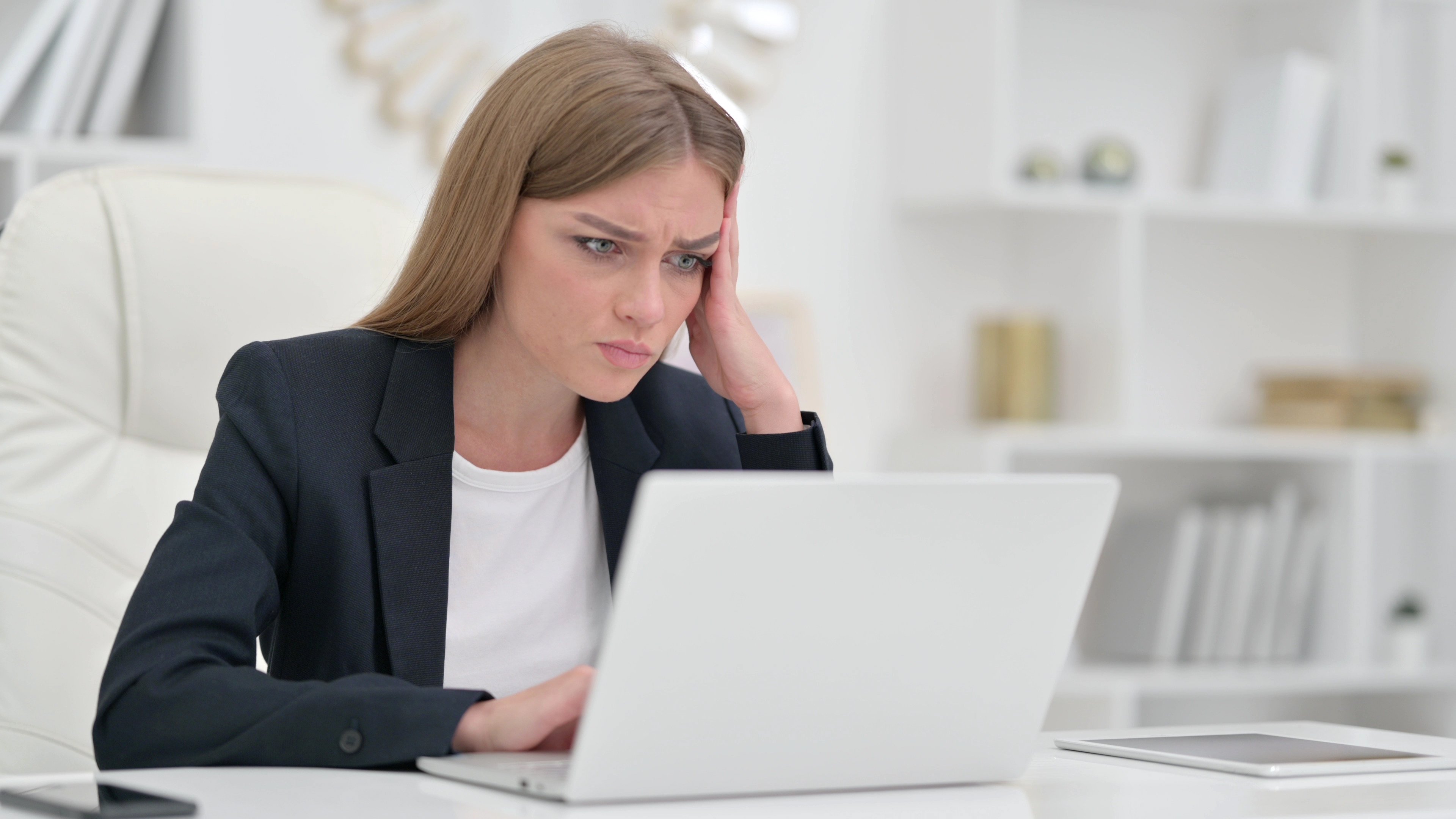 A business person appears deep in thought while looking at a laptop.