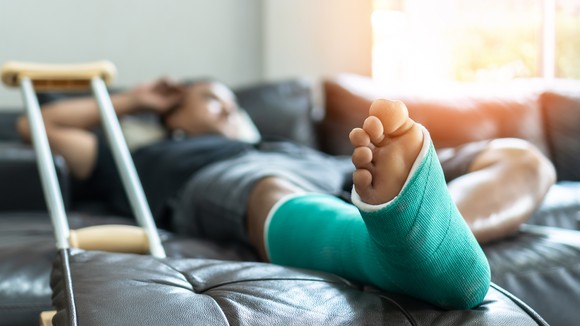 Person in leg cast lying on couch, with a crutch propped up nearby.