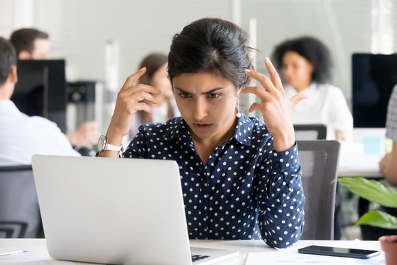 A person frowns and glares at a laptop screen.