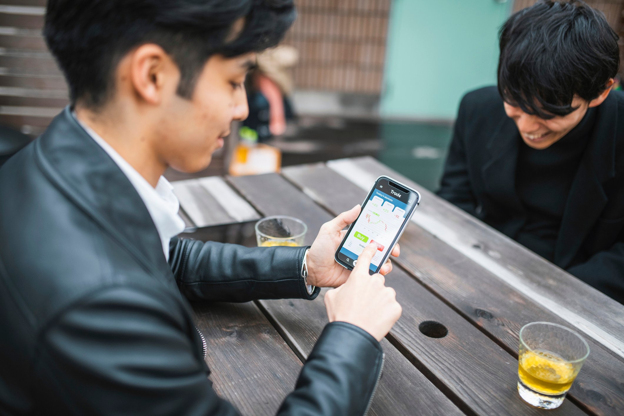 A person sitting at a picnic table outside trading stocks on their phone.
