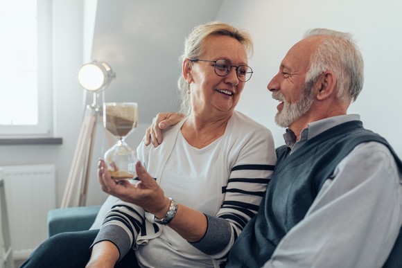 An older couple smiling and holding an hourglass as sand runs through it.