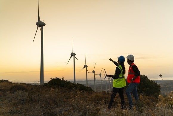 Workers pointing up at a row of windmills.