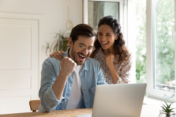 A couple celebrating something while looking at a laptop computer.