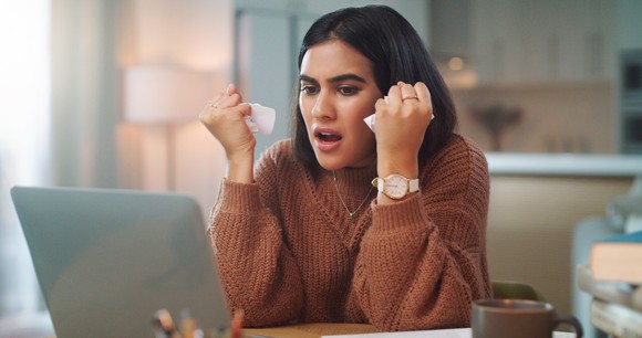 A person with a frustrated expression looking at a laptop.