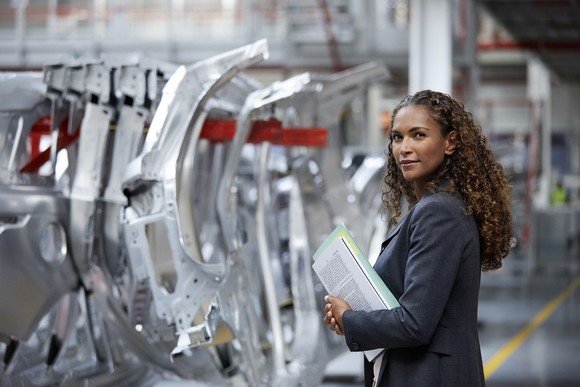 Person holding printed materials standing next to auto chassis components.