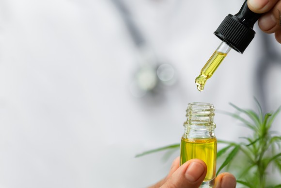 Pair of hands belonging to a medical professional, using a CBD dropper.