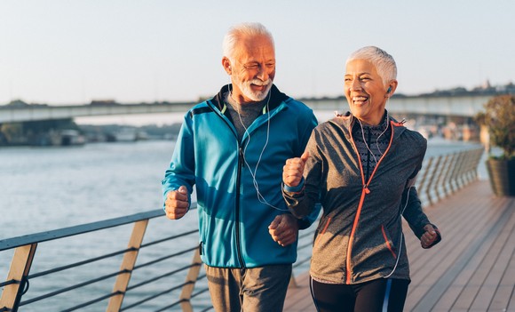 An older couple jogging on a boardwalk.