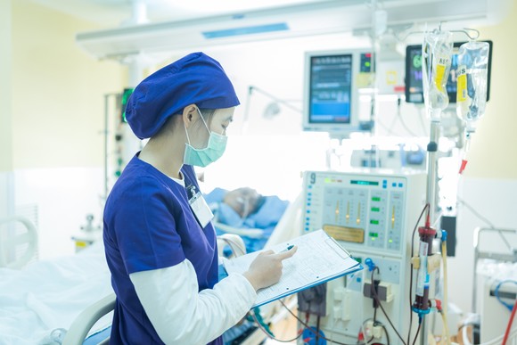 Medical professional with a clipboard in a patient's room in front of a machine.