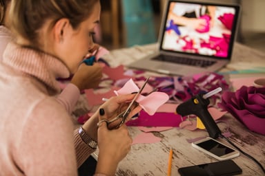 A woman cutting fabric in front of a computer
