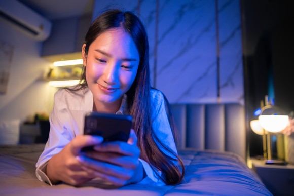 Person checks their phone while lying on bed.