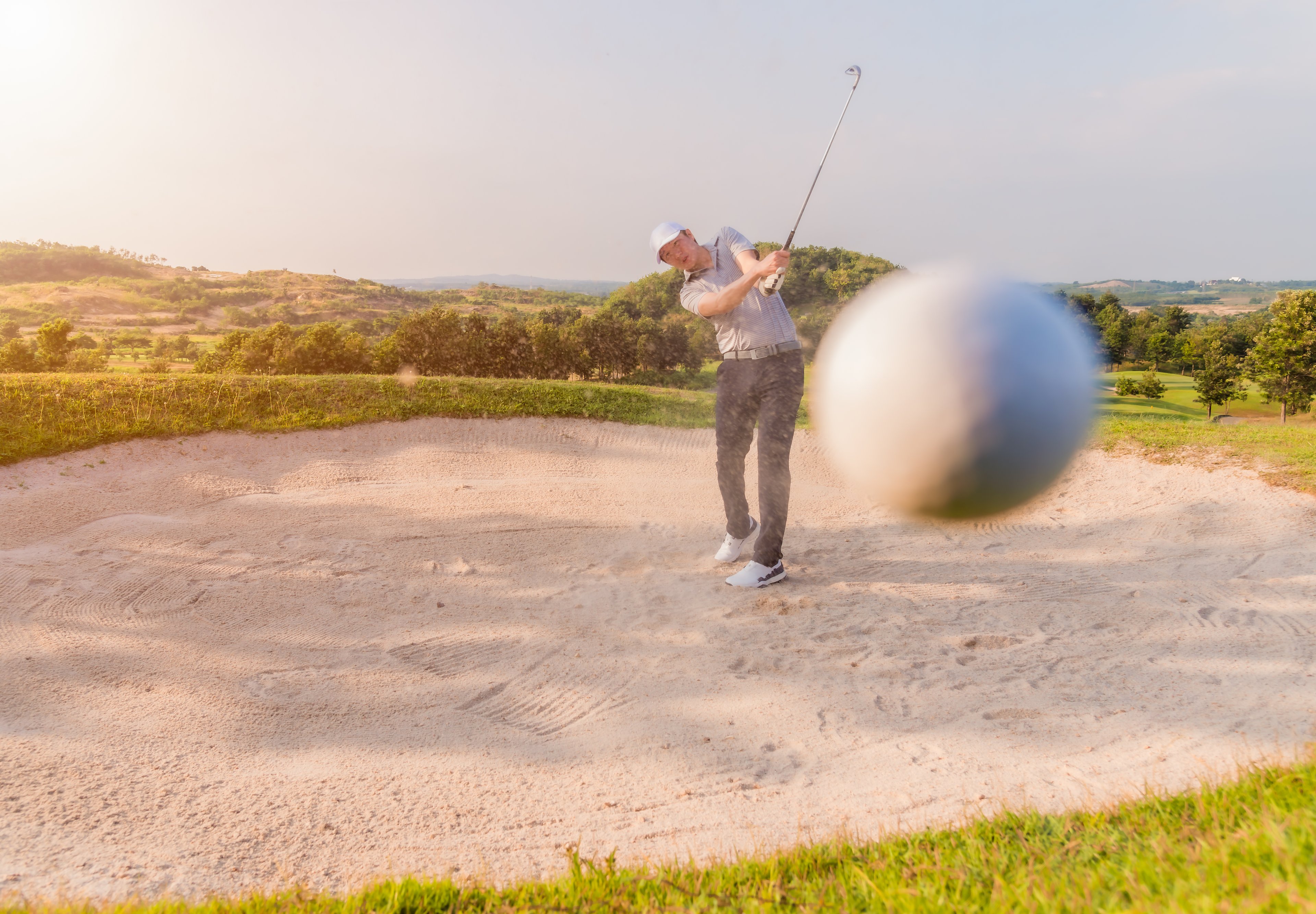 A golfer hits a ball out of a sand trap.