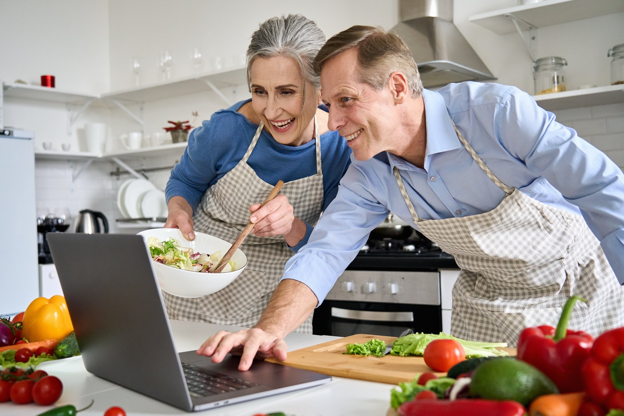 Two people looking at a recipe on a laptop while cooking.