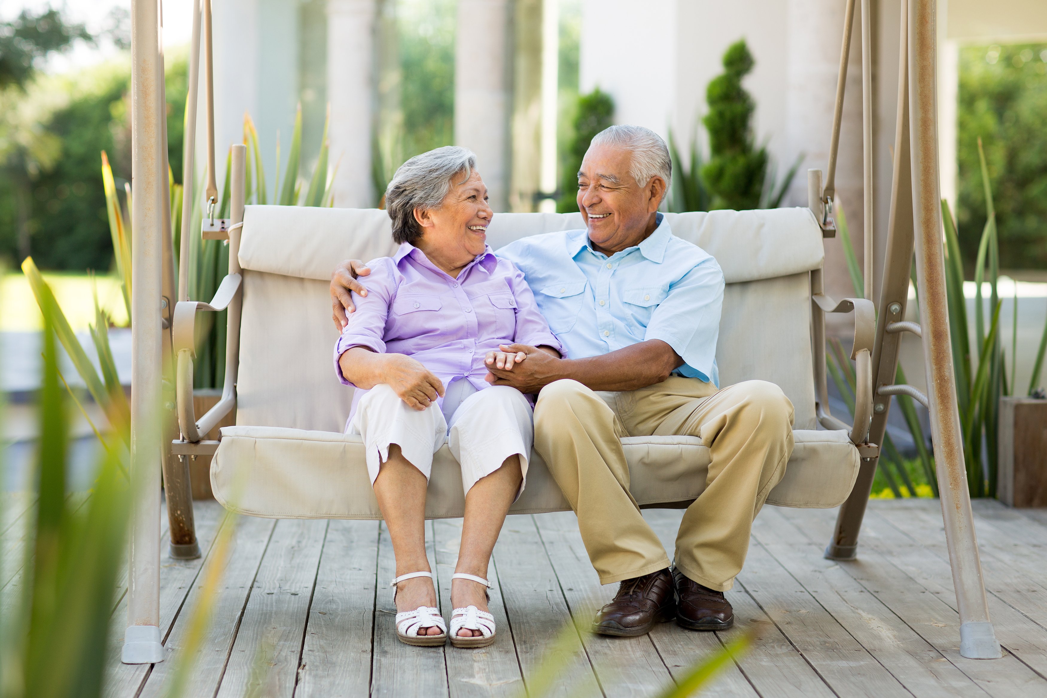 Two people sitting outside on a swing smiling.