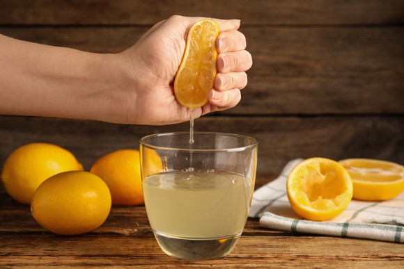 A hand squeezes the juice from a lemon into a large glass.