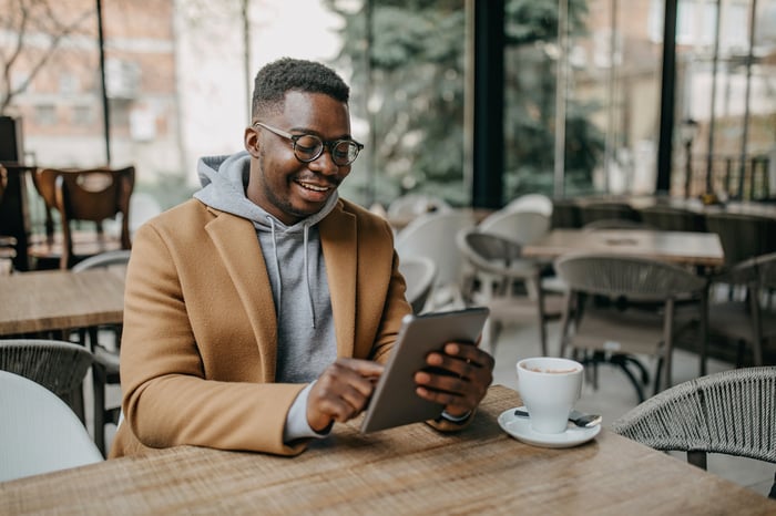 Person at table in coffee shop with tablet and cup.