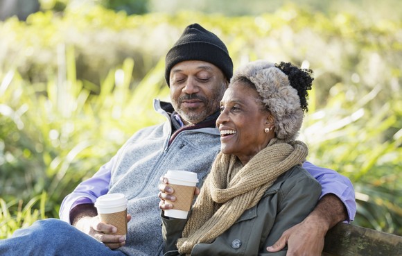 Two people sitting on outdoor bench drinking coffee.