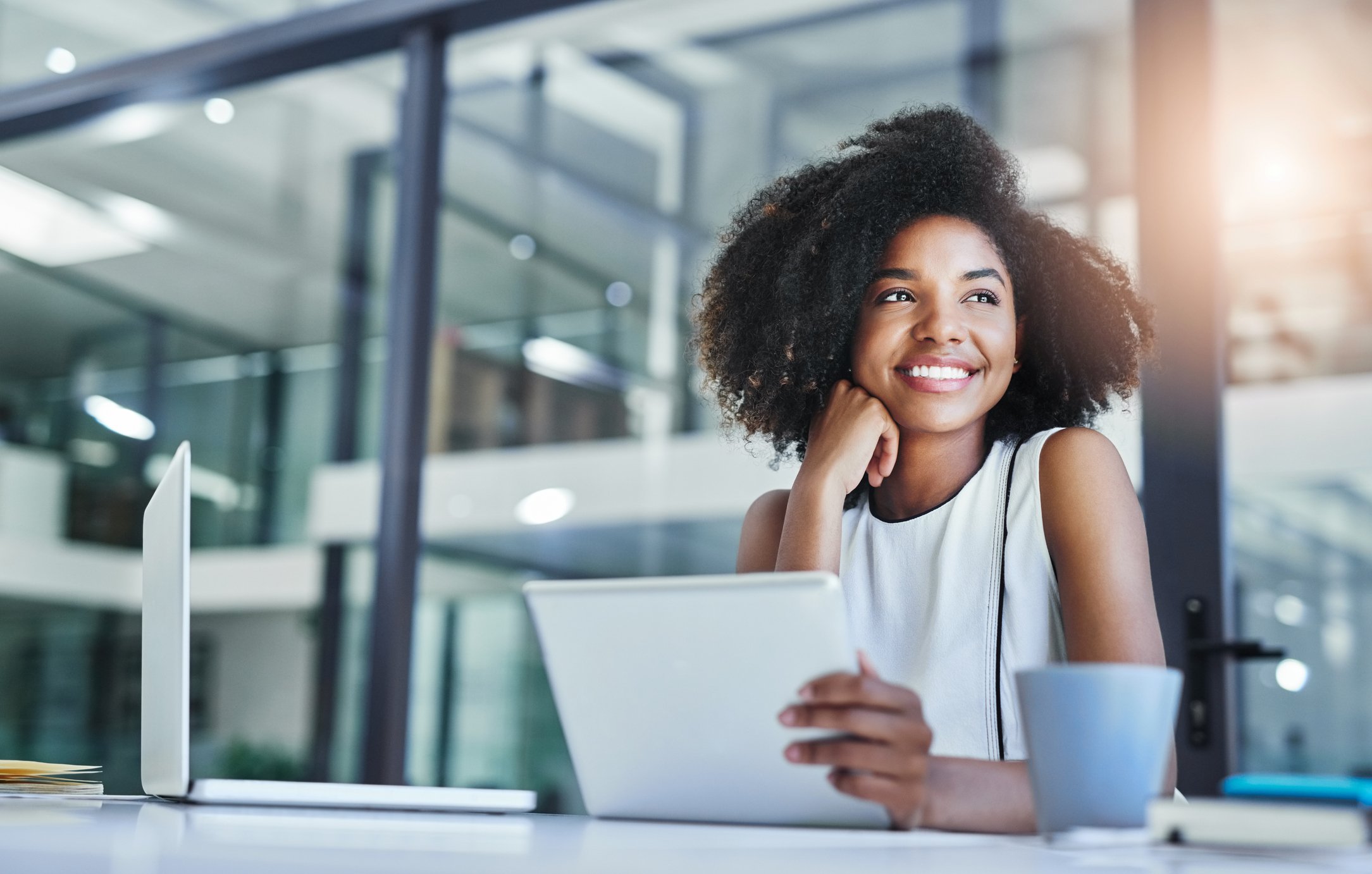 An investor smiles and gazes into the distance while sitting in front of a laptop in a conference room.