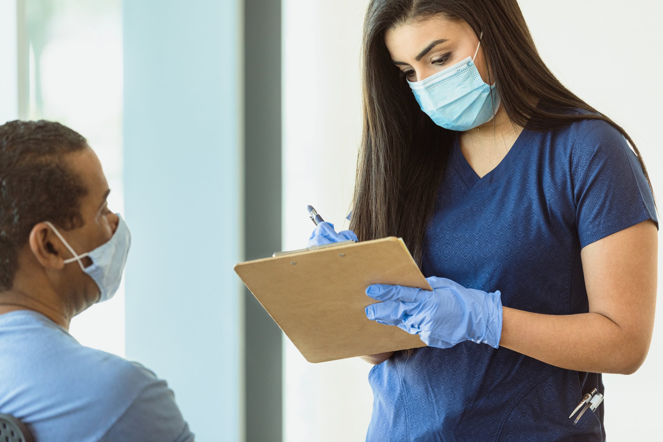 A healthcare worker writes down information about a patient before vaccinating.