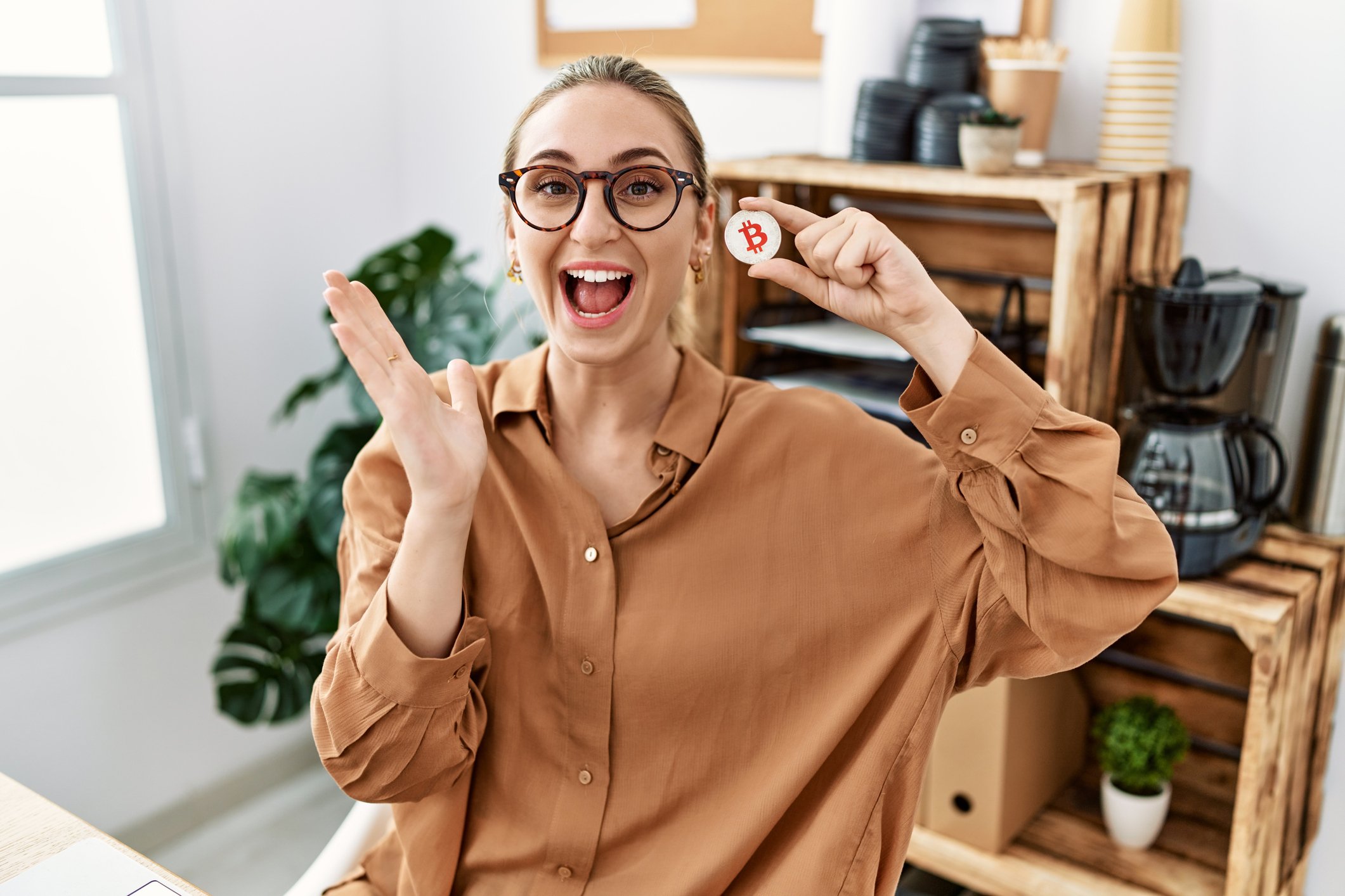 Happy person holdilng up a coin with the Bitcoin logo and smiling.