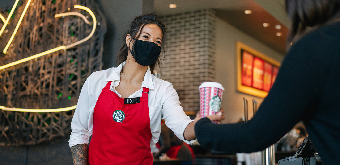 Starbucks barista in a face mask serving a drink.