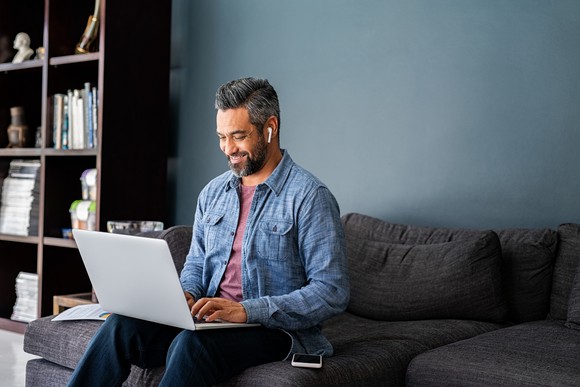 Person smiling at computer on couch with earbuds in.