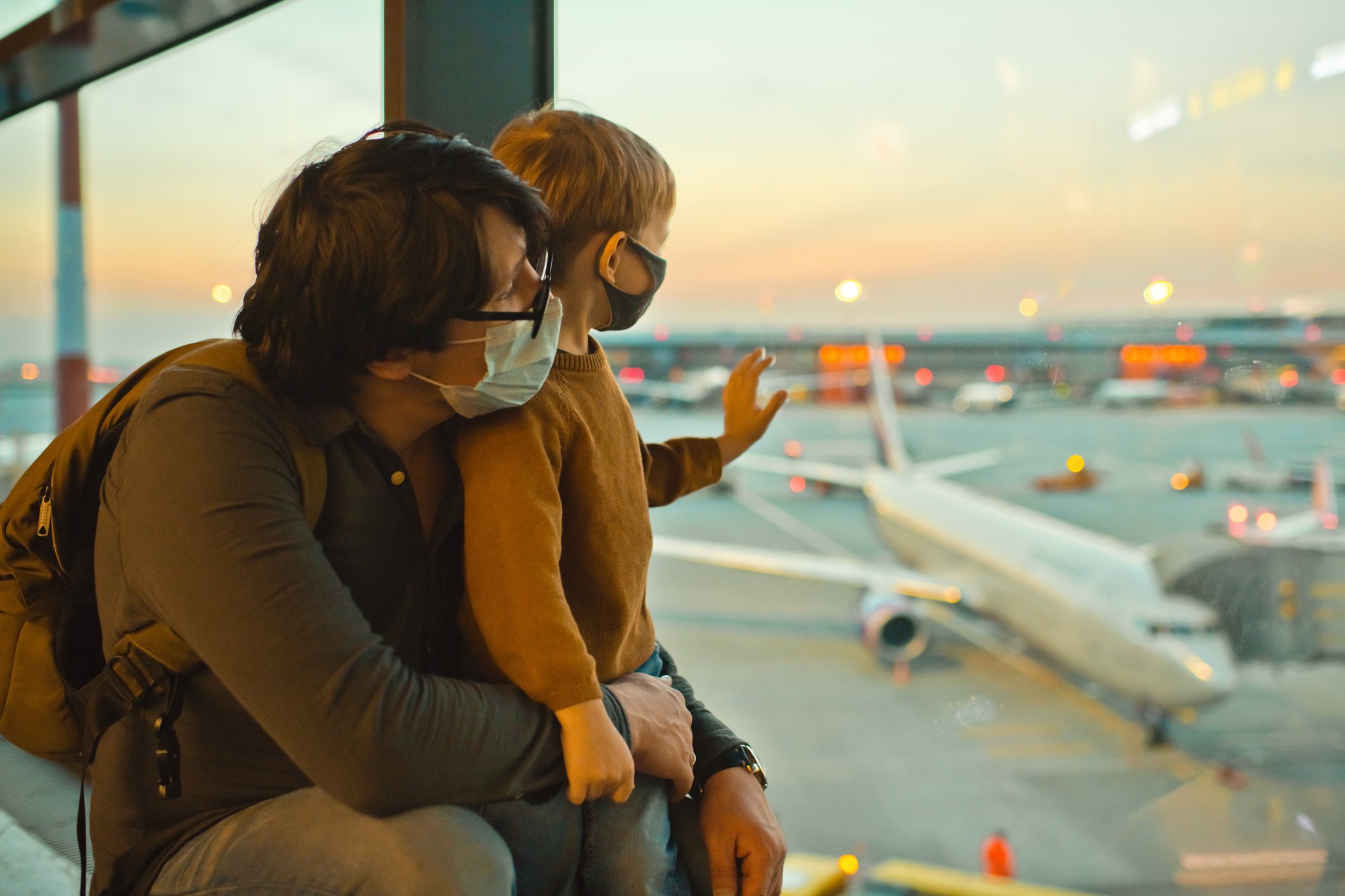 Adult and child looking at airplane from an airport terminal window.