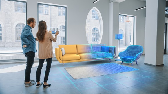 Two people look at a space that has digital furniture arranged in it.