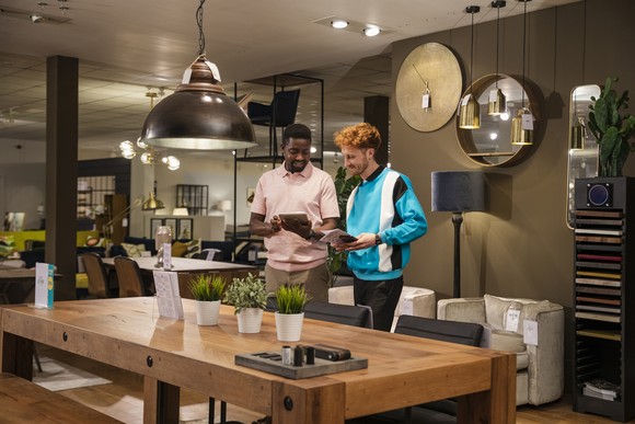Two people standing in a furniture showroom looking at a tablet.