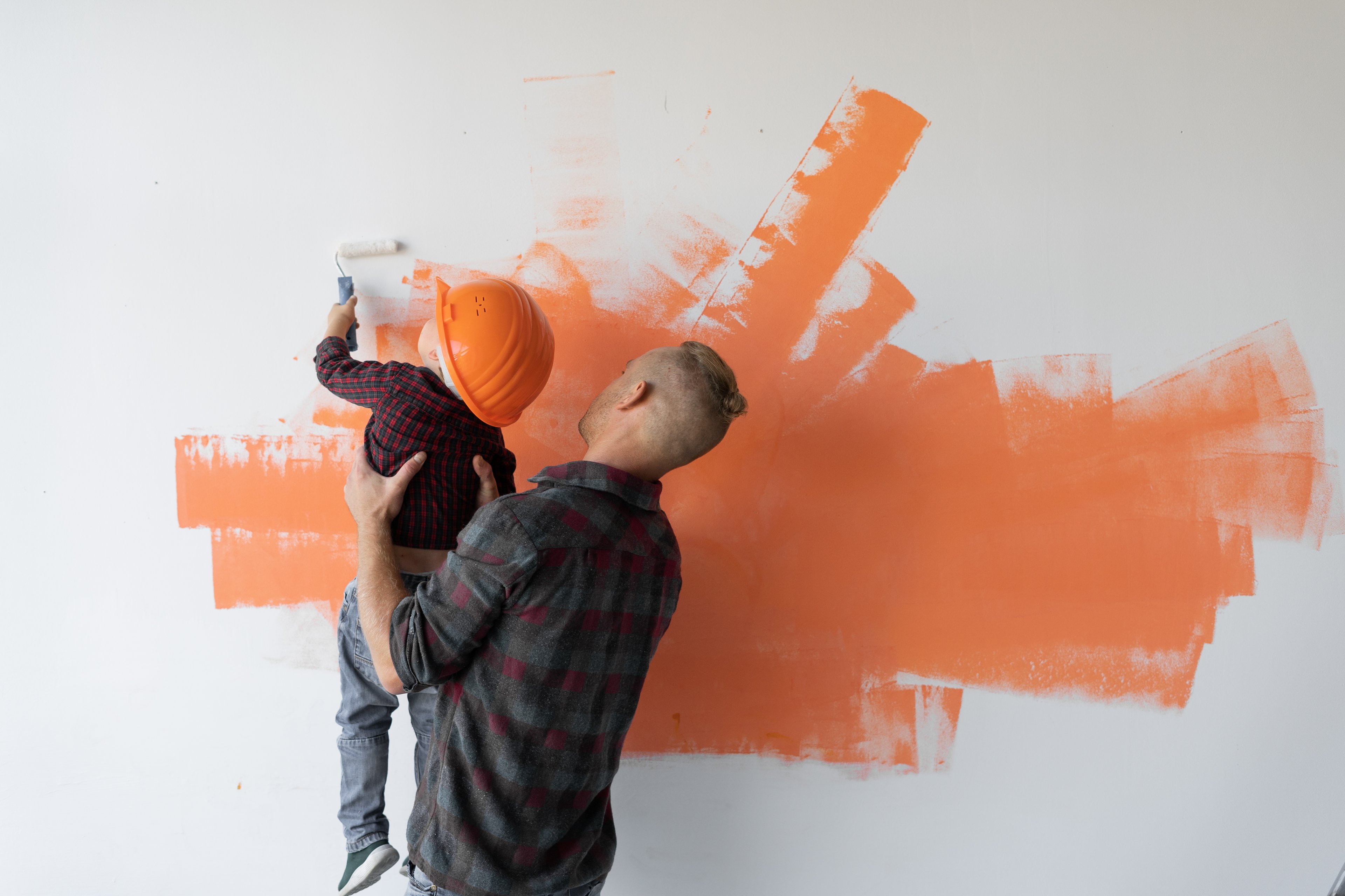 A dad and a boy paint a wall.