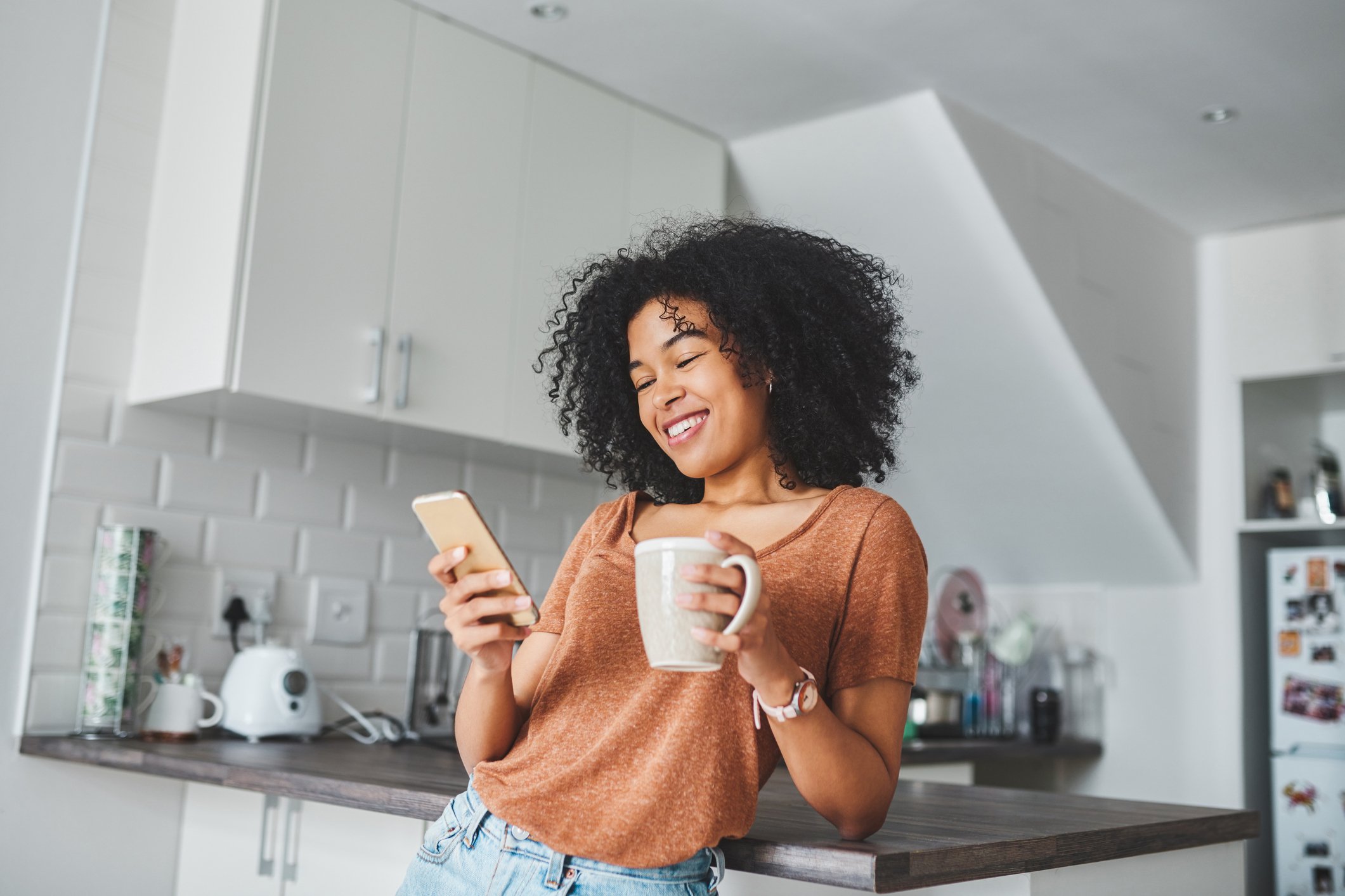 A person smiles and looks at a phone in a kitchen. 