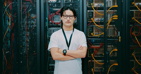 Software engineer posing in front of a rack of servers.