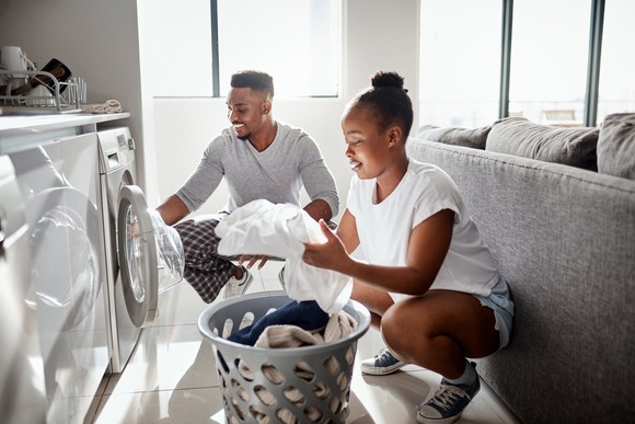 Two people taking laundry out of the dryer in front of a couch. 