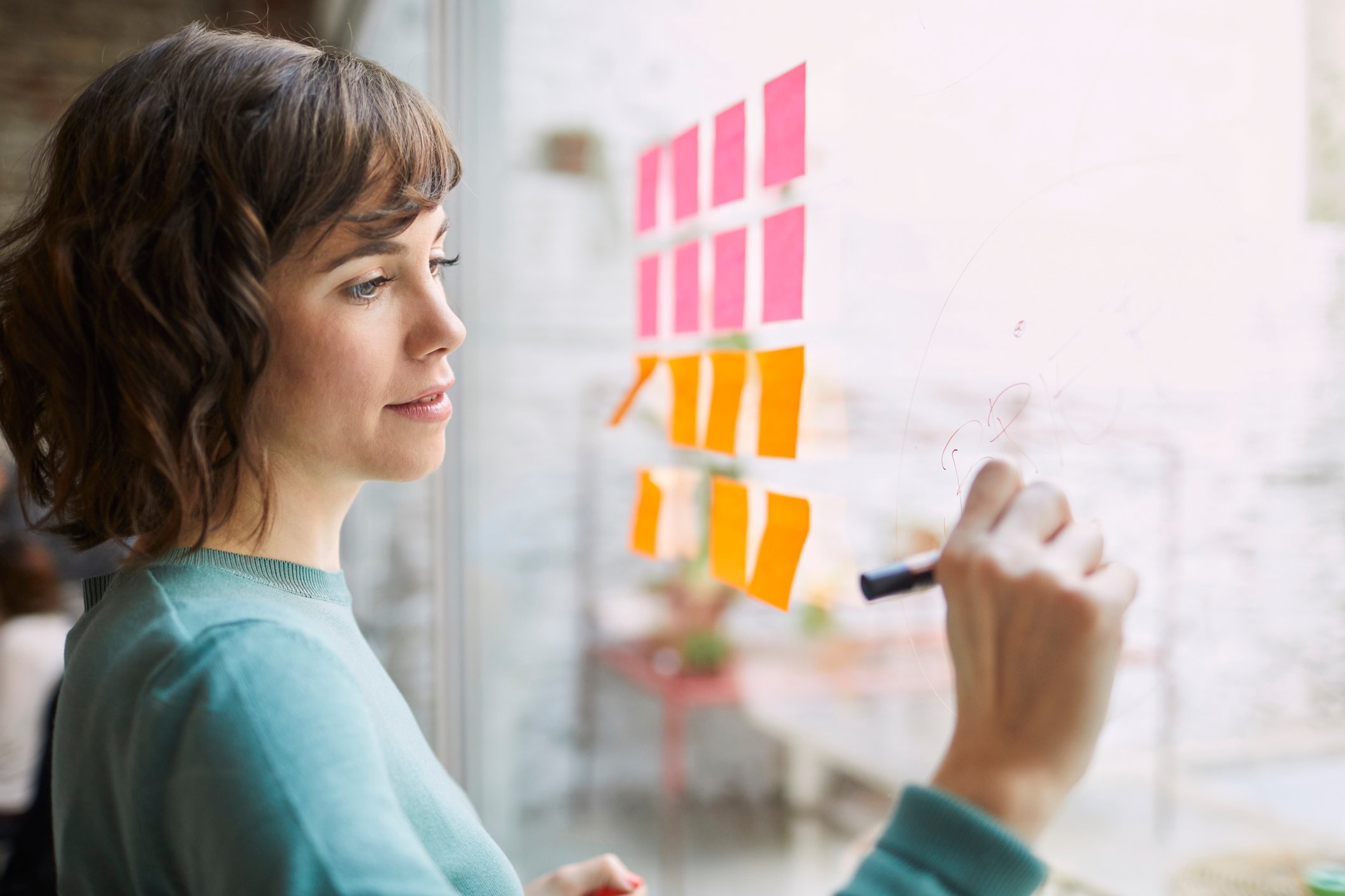 A person brainstorming ideas on a wall with a marker and sticky notes. 