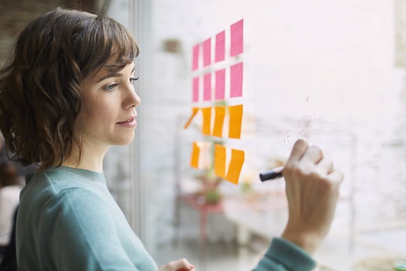 A person brainstorming ideas on a wall with a marker and sticky notes. 