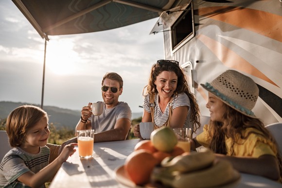 A family enjoys a meal outside their RV camper.
