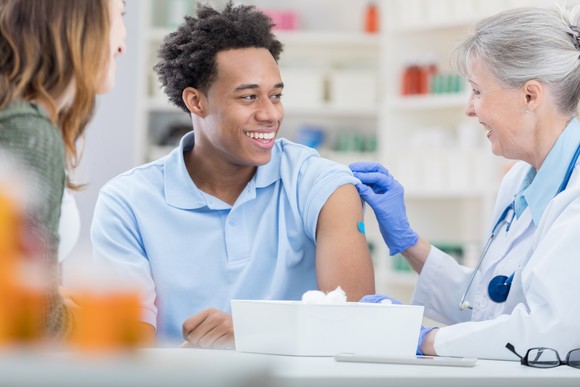 A person in a pharmacy with their sleeve rolled up smiles at a healthcare worker.