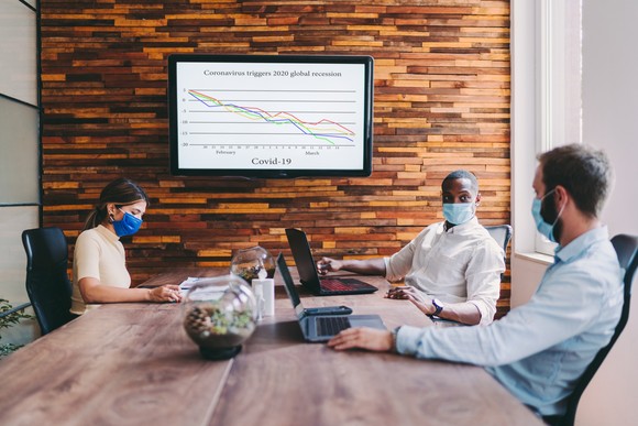Three people sitting at a conference table wearing masks.