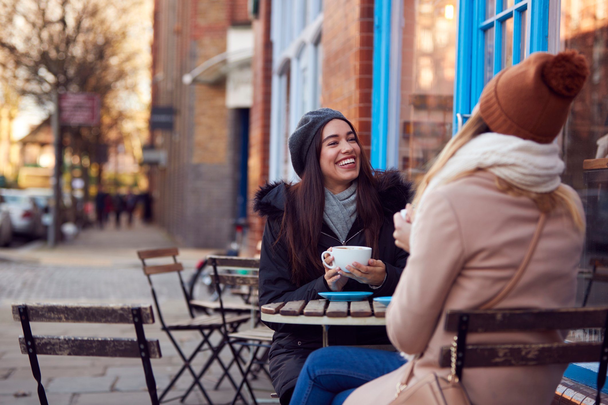 Two people smile while chatting in front of a cafe. 