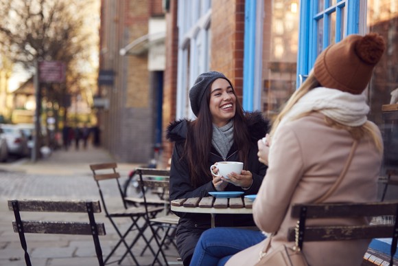 Two people smile while chatting in front of a cafe. 