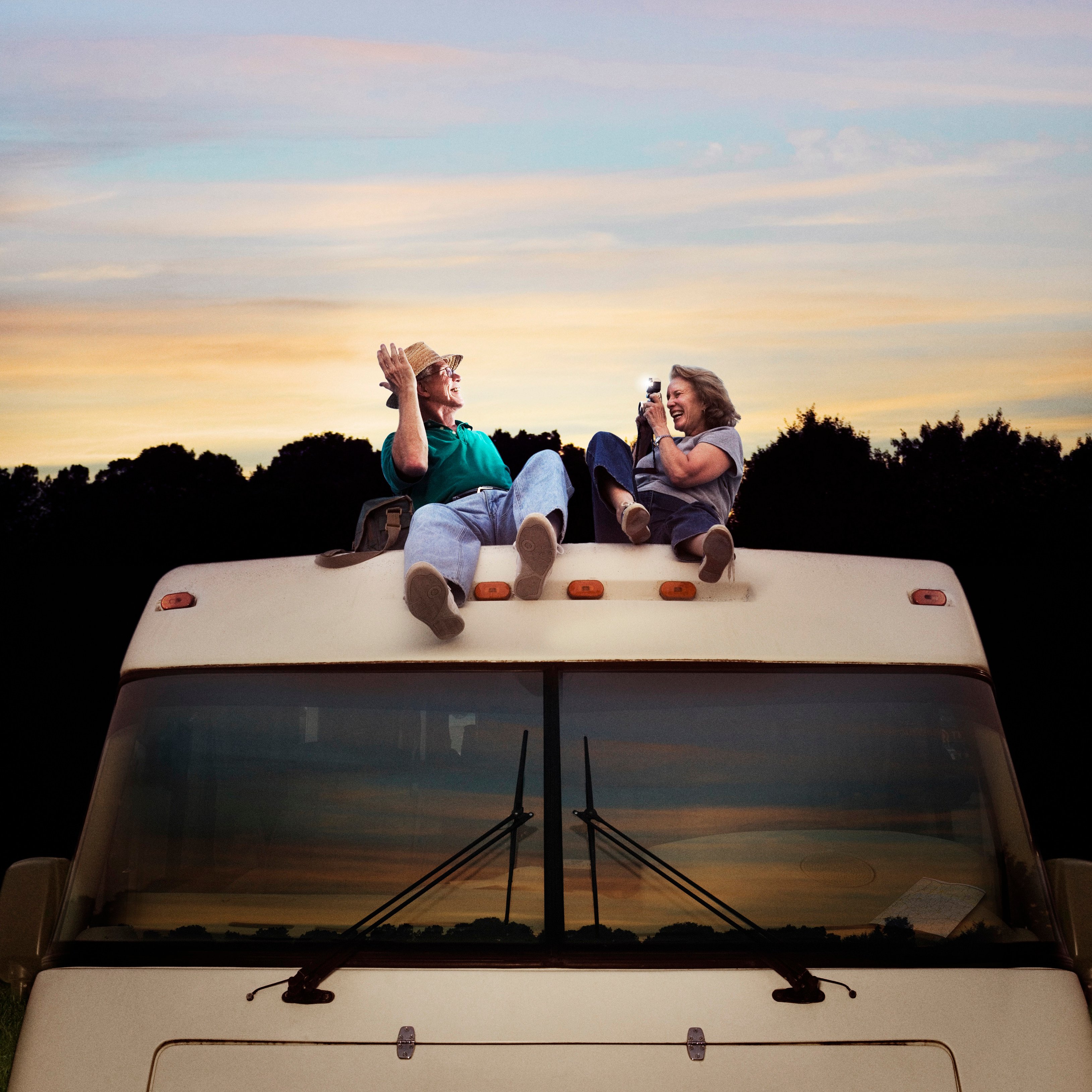 A man and woman sit on the roof of an RV. 