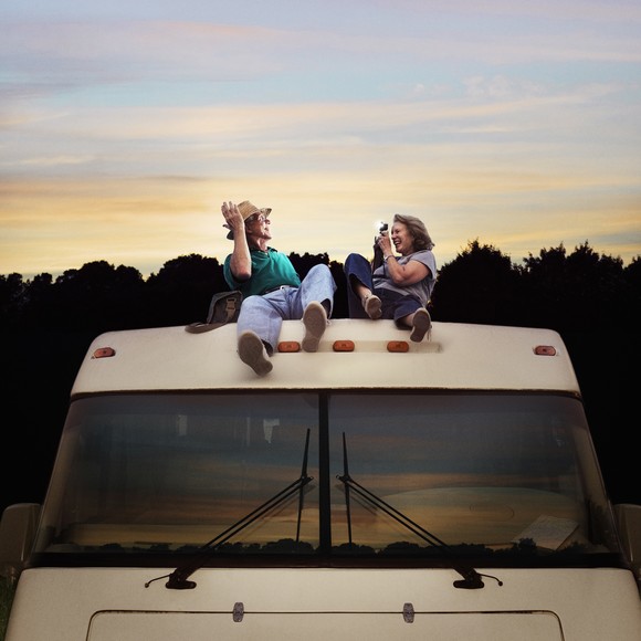 A man and woman sit on the roof of an RV. 